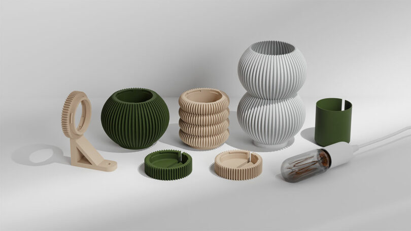 A collection of ribbed, spherical, and cylindrical green and beige 3D-printed objects on a white background includes planters, light bulb covers, a toothbrush holder, and the innovative STAK Modular Lamp.