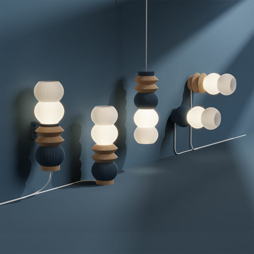 Introducing the STAK Modular Lamp collection: Modern pendant and wall-mounted lights grace a blue wall, showcasing elegantly stacked spherical and conical shapes in neutral tones.