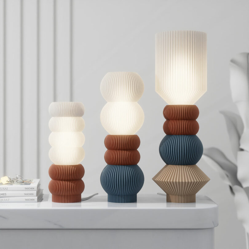 Three STAK Modular Lamps with stacked, ribbed designs in white, blue, and brown sit on a white surface against a plain background.