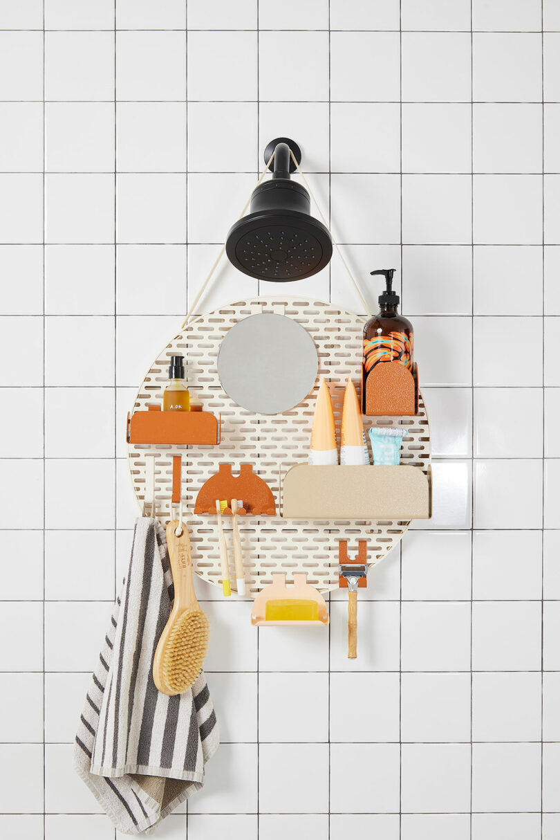 Shower wall organizer with various toiletries and grooming items, including bottles, tubes, a razor, and a brush, hanging on a tiled bathroom wall under a showerhead.