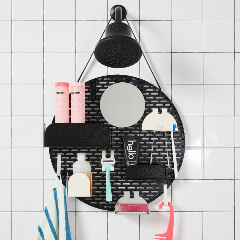 A black shower caddy hanging under a showerhead on a tiled wall, holding various toiletries including shampoo bottles, a razor, a toothbrush, toothpaste, soap, and a washcloth.