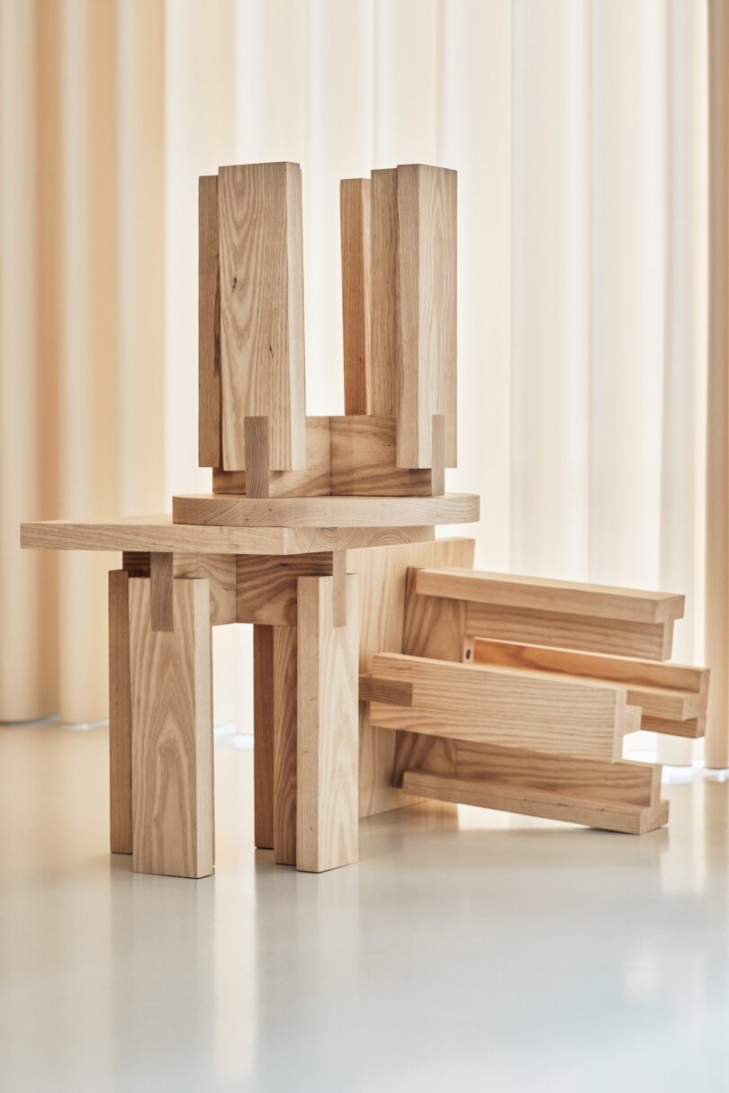 Wooden furniture pieces composed of interlocking blocks, styled in a minimalist design, positioned in front of beige curtains