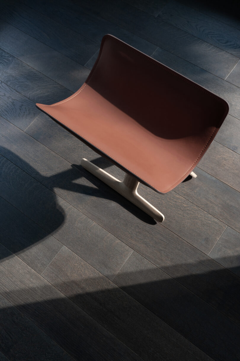 A brown leather chair with a wooden base is placed on a dark wooden floor, casting shadows under soft lighting