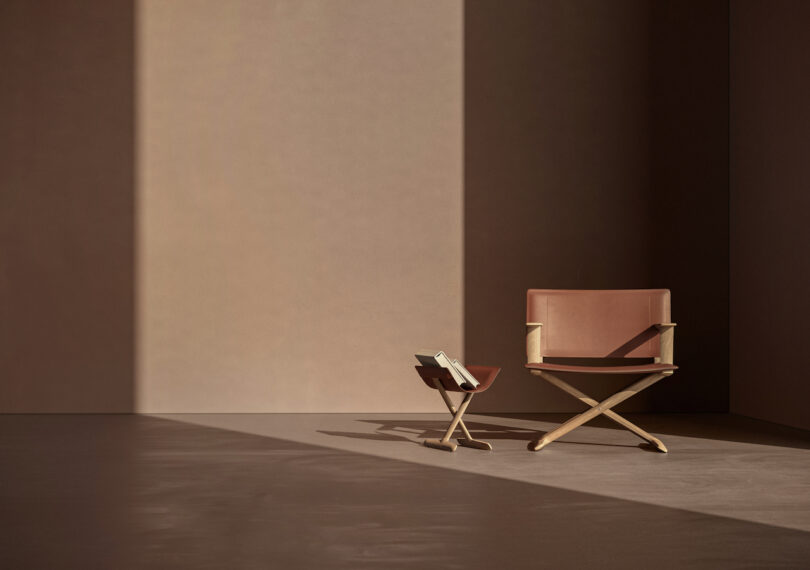 A minimalist scene with a brown leather chair and a small wooden side table holding a book, both positioned against a plain, sunlit wall