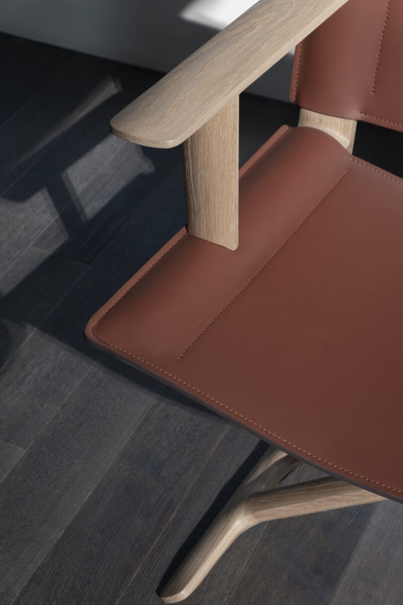 A close-up of a modern chair, featuring a wooden frame and a brown leather seat