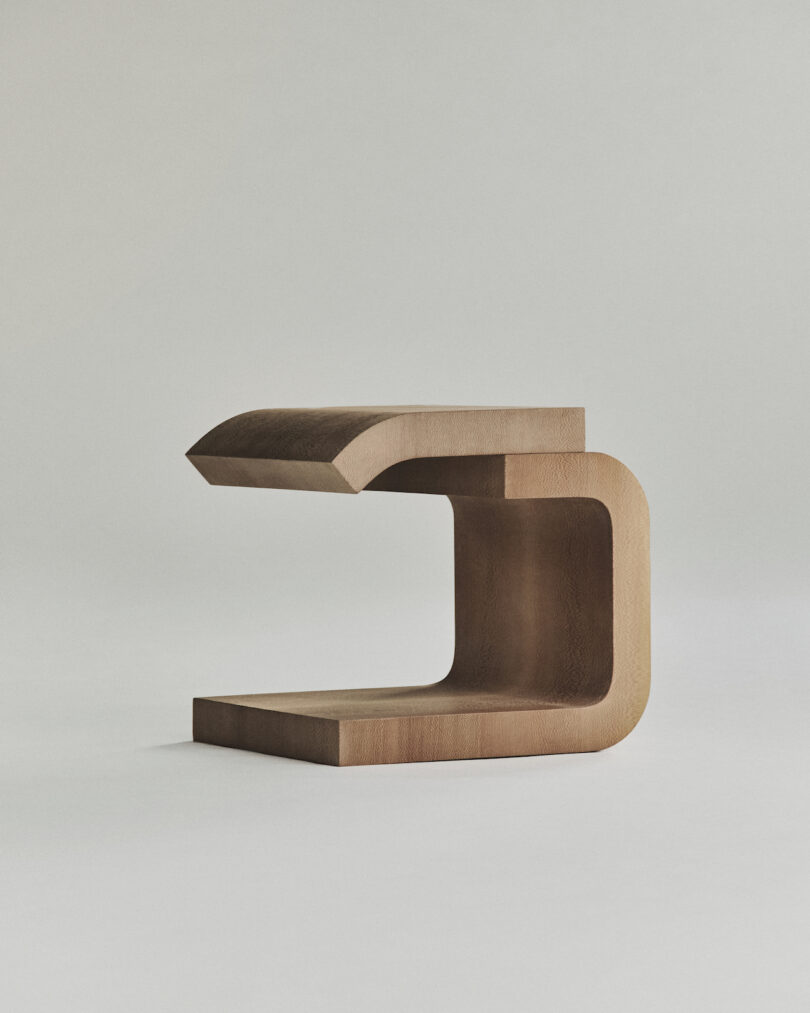 A minimalist, wooden, C-shaped side table with clean lines and a natural wood finish.