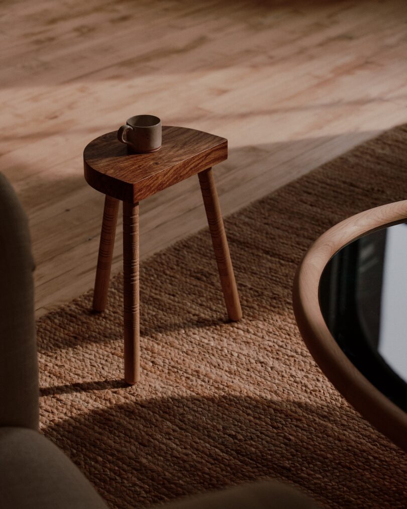 Small wooden table with a mug on top, placed on a textured brown rug in a sunlit room.