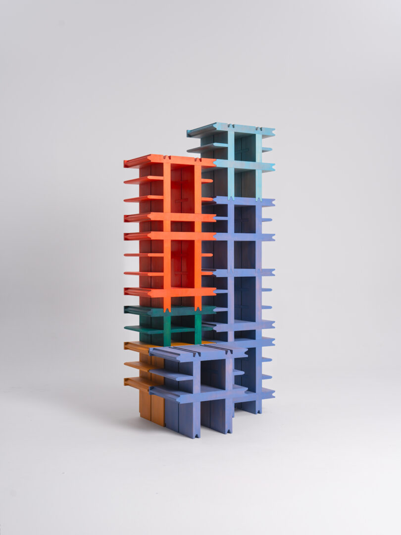 A tall, modern bookshelf composed of four sections in blue, red, green, and yellow, standing against a plain, white background