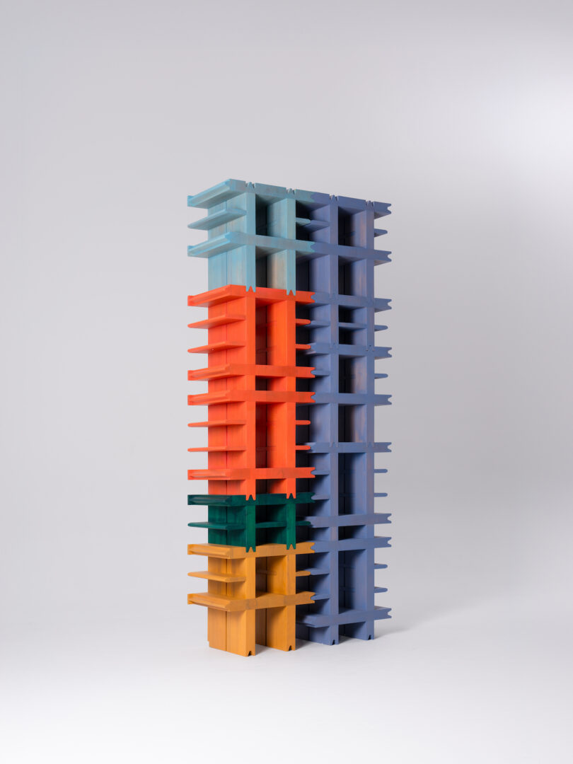 A tall, modern bookshelf composed of four sections in blue, red, green, and yellow, standing against a plain, white background