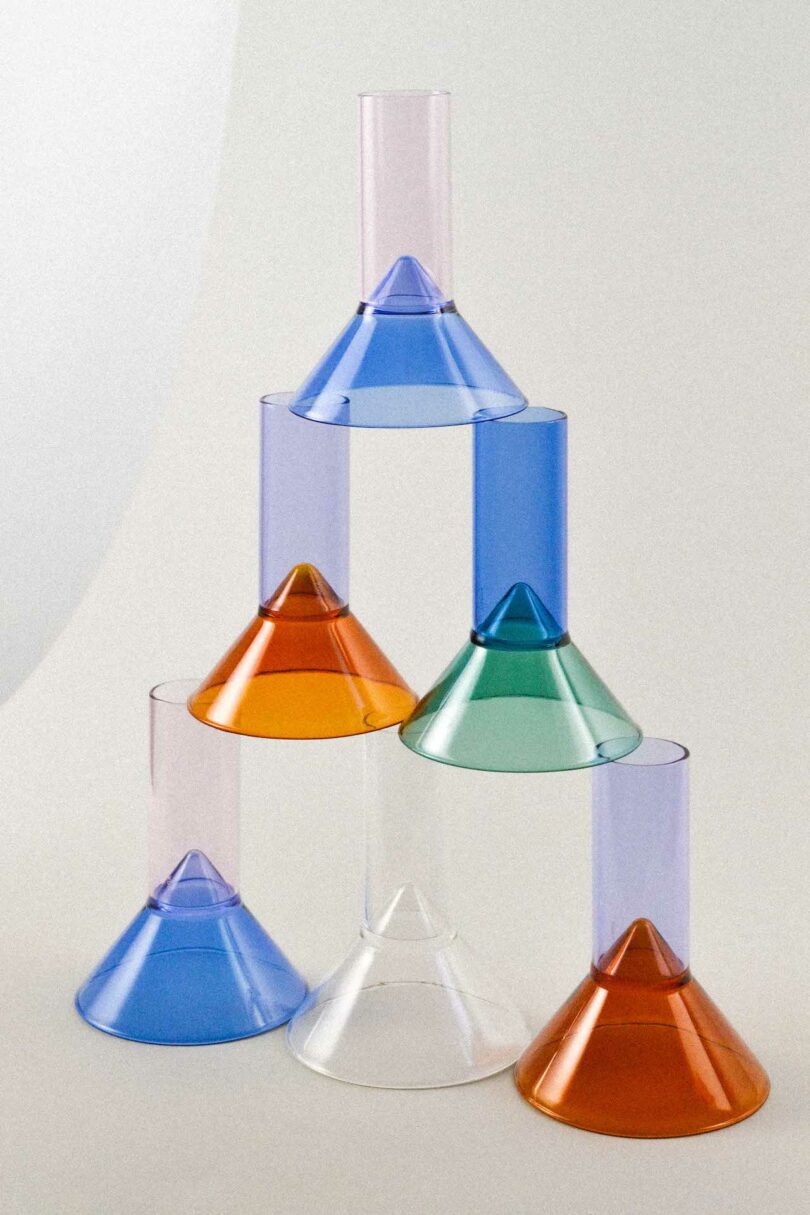 A pyramid constructed of colorful, translucent conical glasses, featuring blue, green, orange, purple, and clear segments against a light background.