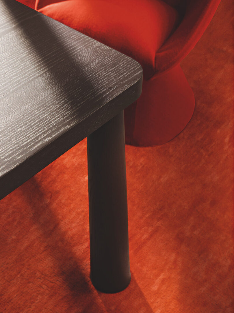 Close-up of a black wooden table leg beside a red carpet and part of a red upholstered chair