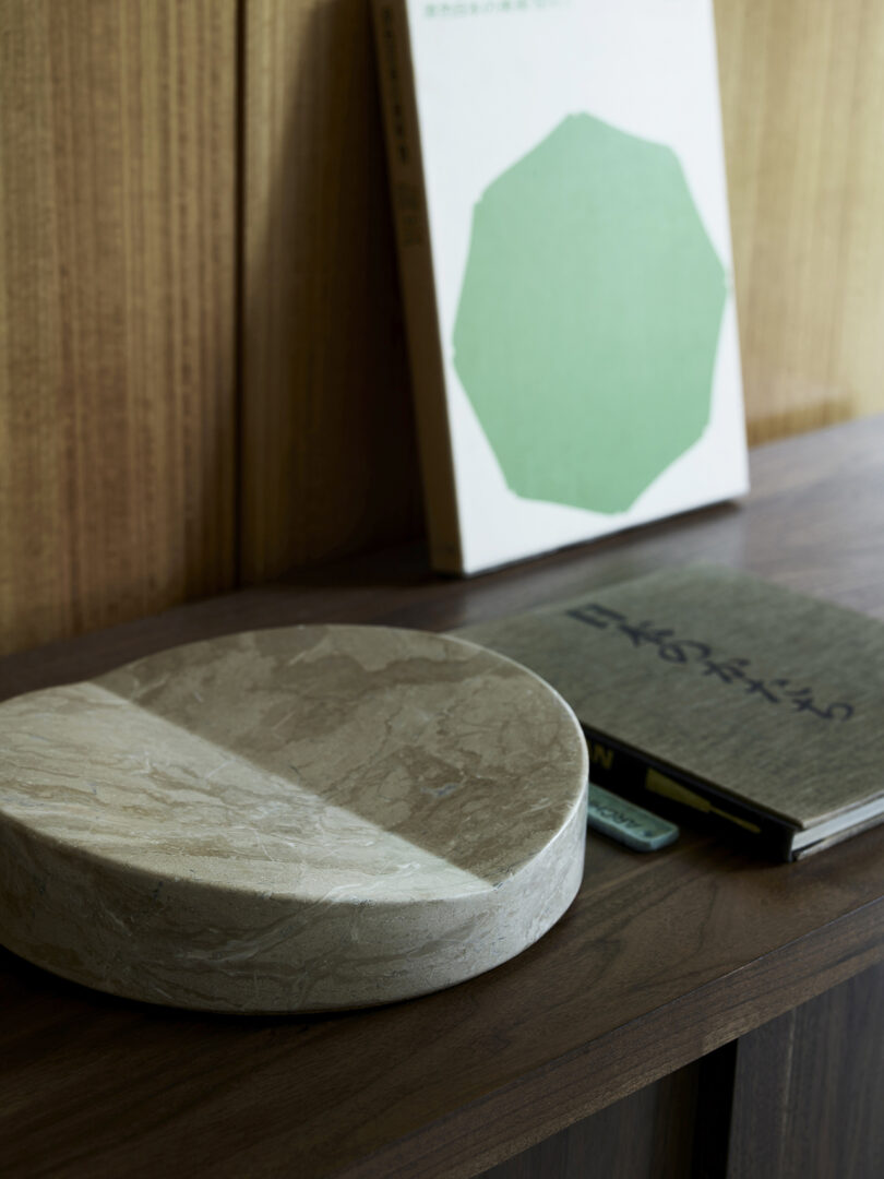 A round stone object on a wooden shelf, with two books nearby. One book has a green shape on the cover.