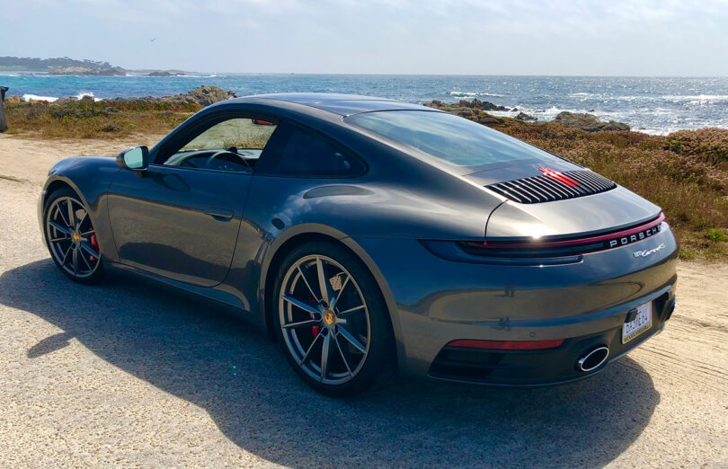 A sleek gray sports car, reminiscent of Dan Harden's innovative designs, sits elegantly near a rocky coastline with the vast ocean stretching into the distance.