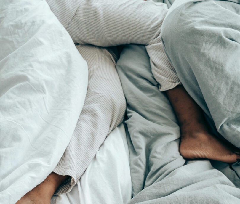 The feet and legs of two people rest intertwined beneath white and gray sheets, a serene moment that might inspire even Dan Harden's artistic eye.