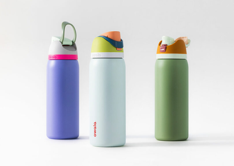 Three colorful Owala water bottles designed by Dan Harden are displayed against a plain background. They feature vibrant blue, green, and teal colors, each boasting unique cap designs that blend functionality with style.