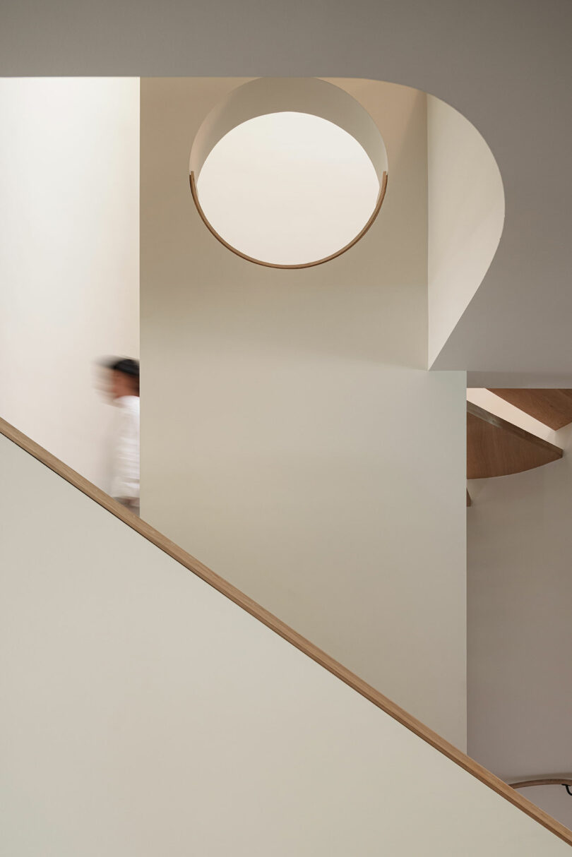 A person walks down a staircase with minimalist design and geometric shapes, including a circular cutout and clean lines.