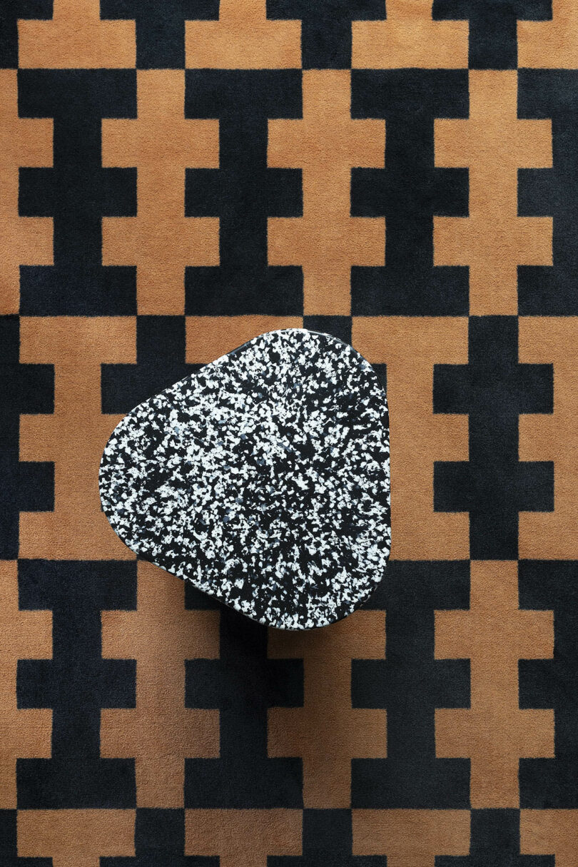 Black and white speckled stone table on a geometric-patterned brown and black rug.