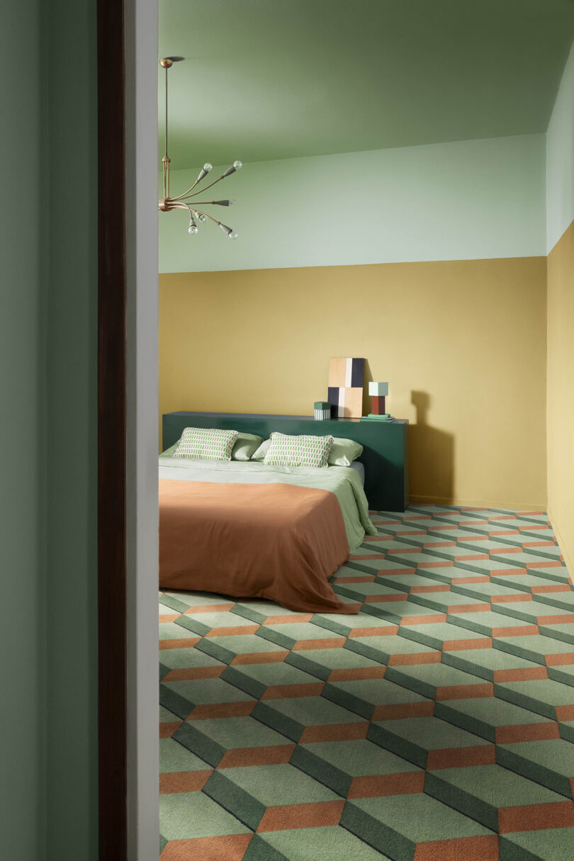 Geometric patterned bedroom with green and brown tones, featuring a modern light fixture, a brown bedspread, and decorative rug.