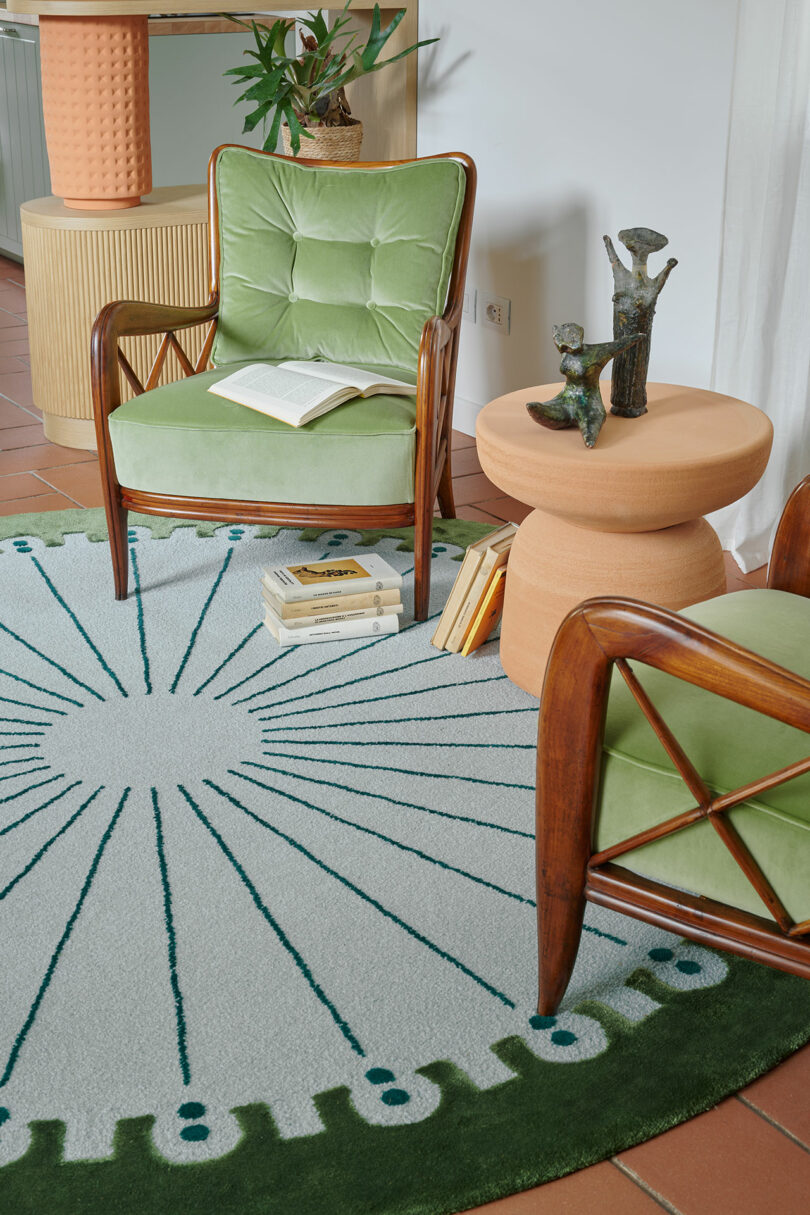 Two green chairs and a round side table on a patterned rug, with an open book and decorative items.