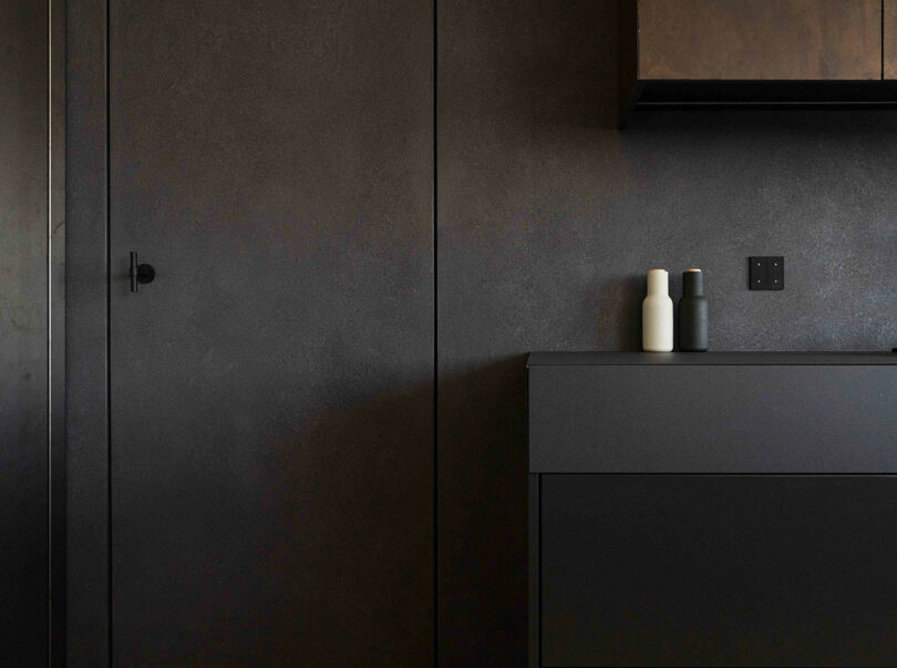 Minimalist kitchen with dark cabinets, a matte black wall, and two ceramic bottles on the counter.