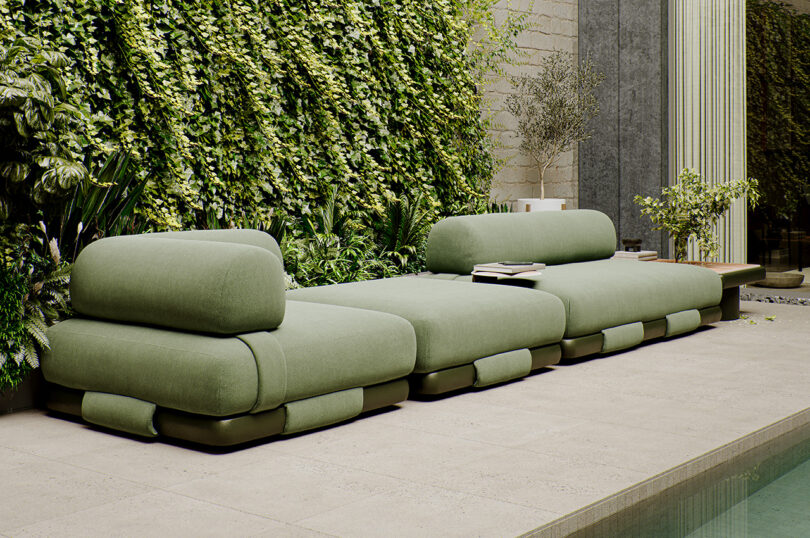 Modern green sofa by a wall covered in lush plants, adjacent to a poolside setting.