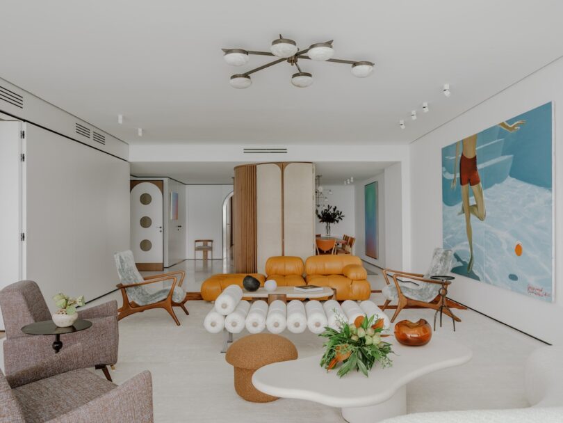 Modern living room with a variety of chairs, a mustard-colored couch, a coffee table, an abstract painting, and a ceiling light fixture. Neutral tones with a pop of color from the art and furnishings