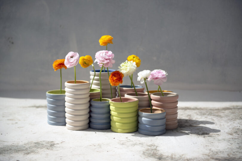 Colorful flowers in simple, textured ceramic vases arranged on a light surface with a gray background