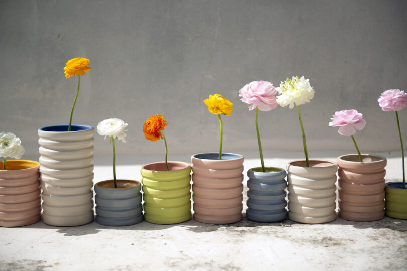 Colorful flowers in tall, ribbed ceramic vases arranged in a line on a concrete surface