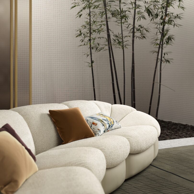 A cream-colored couch with decorative pillows is situated in a room with bamboo plants and a textured wall