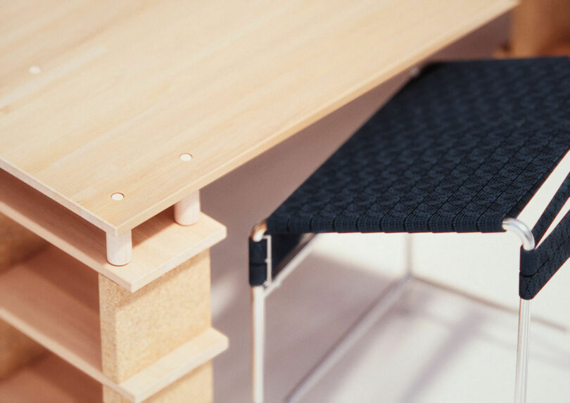 Close-up of a wooden table corner with visible dowels and a textured black chair with metal legs beside it