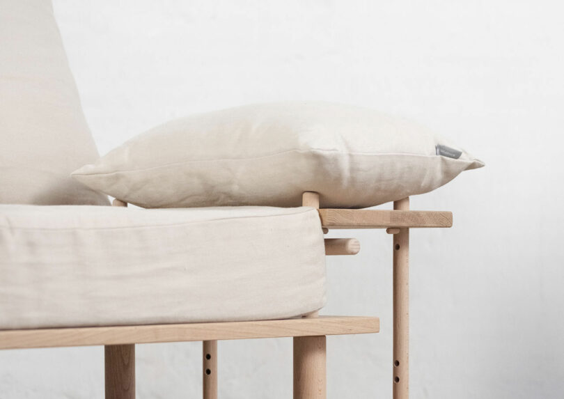 A minimalist chair with a beige cushion and pillow on a wooden frame, set against a plain white background