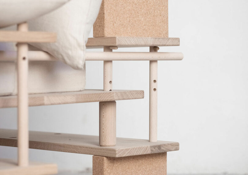 Close-up of a wooden bed frame with shelves, featuring interlocking vertical and horizontal wooden planks and a visible pillow on top