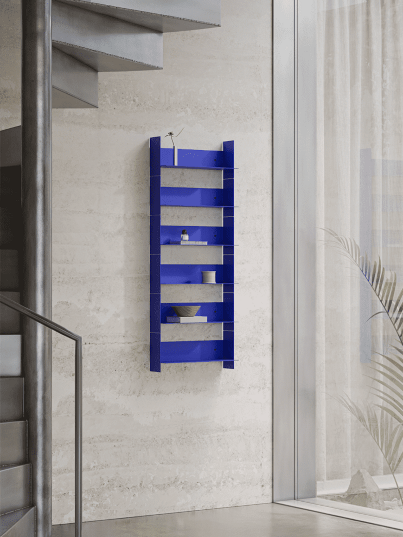 Blue wall-mounted shelf holding small decorative items in a modern, minimalist room with a stair railing and large window