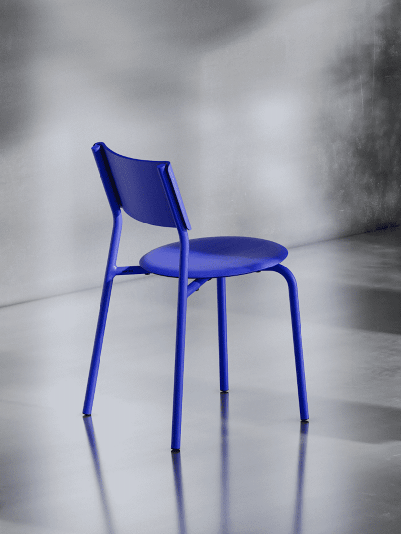 A modern blue chair with a simple design on a reflective gray surface, angled to show the back and side