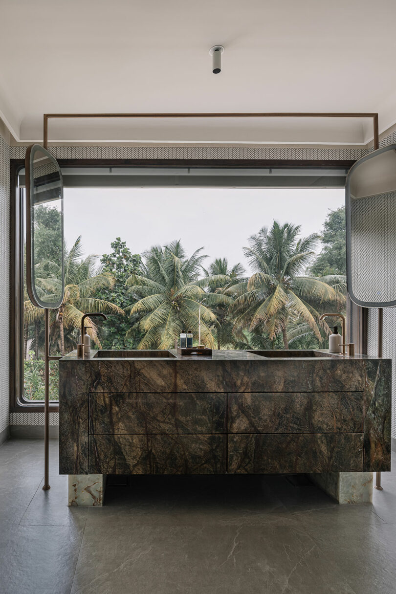 Luxurious bathroom with a large marble vanity, twin mirrors, and a lush tropical view through a floor-to-ceiling window.