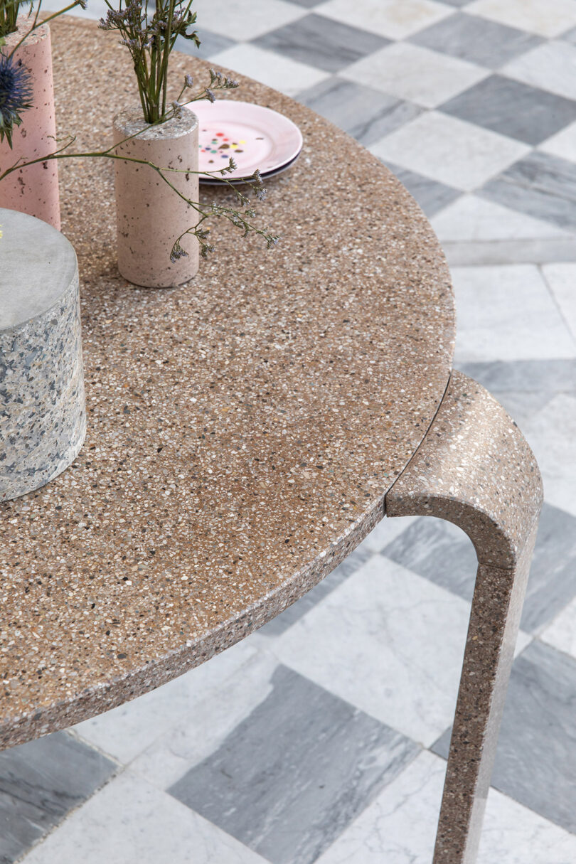 Round stone table with vases and a pink plate on a checkered floor.