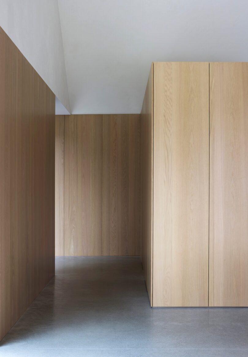 Minimalist interior with light wood paneled walls, concrete floor, and simple geometric design.