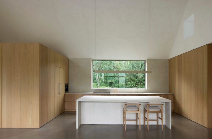 Minimalist kitchen with wooden cabinets, a large window, and a white island with two stools.