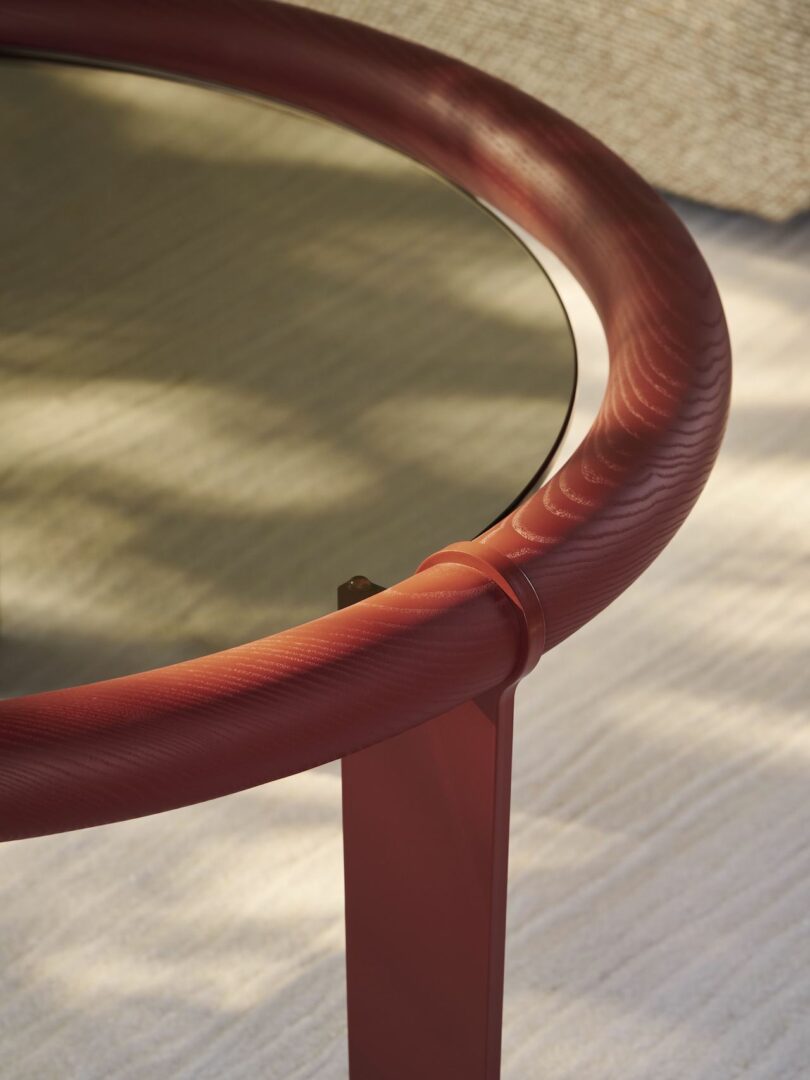 Close-up of a round table with a red metal frame and a glass top, casting a shadow on a light-colored surface