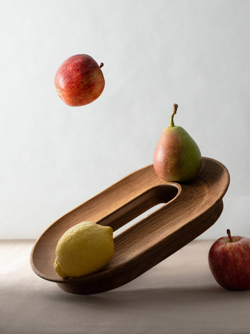 Floating apple above a wooden tray with a lemon and pear, another apple and pear nearby, on a neutral background