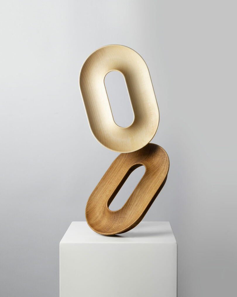 Two fruit vessels balanced vertically on a white pedestal against a gray background