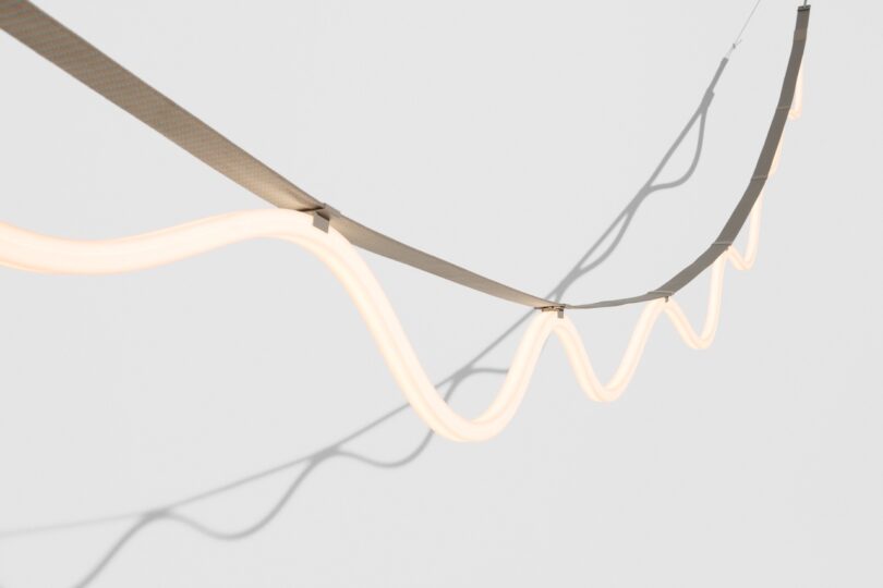 A wavy, illuminated string of lights suspended against a plain gray background