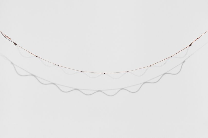 A wavy, illuminated string of lights suspended against a plain gray background