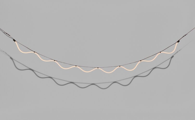 A wavy, illuminated string of lights suspended against a plain gray background