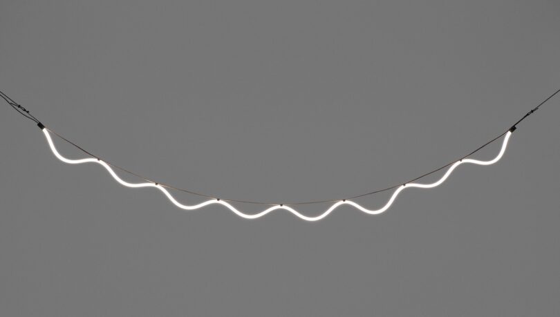 A wavy, illuminated string of lights suspended against a plain gray background