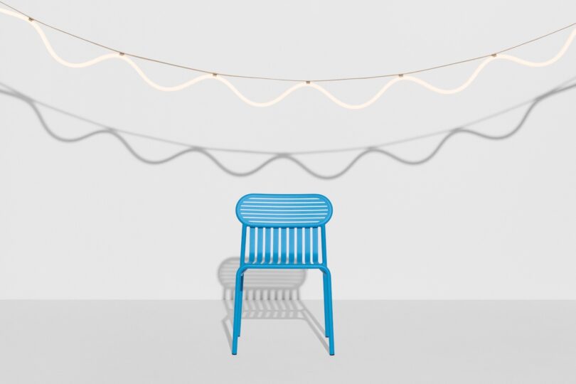 A blue metal chair sits against a light grey background with two wavy, white cords casting shadows above