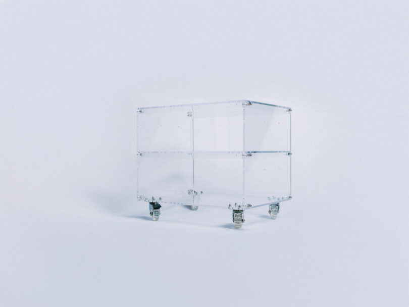 A transparent glass box on caster wheels stands against a plain white background