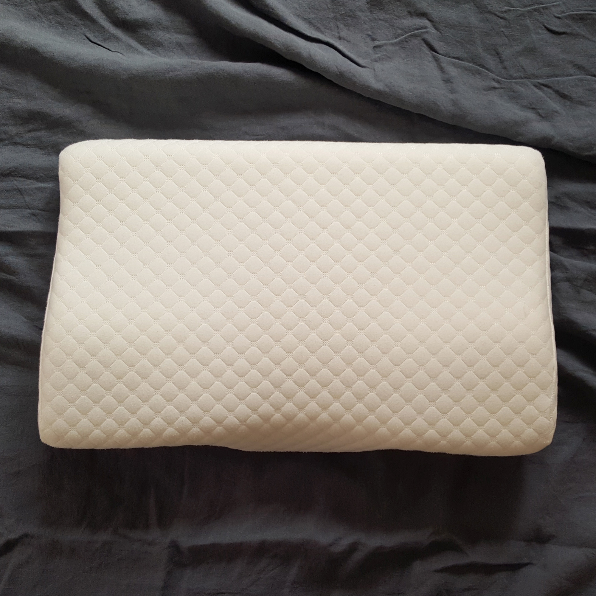 The Kally Sleep Neck Pain pillow being tested on a bed with grey bedlinen