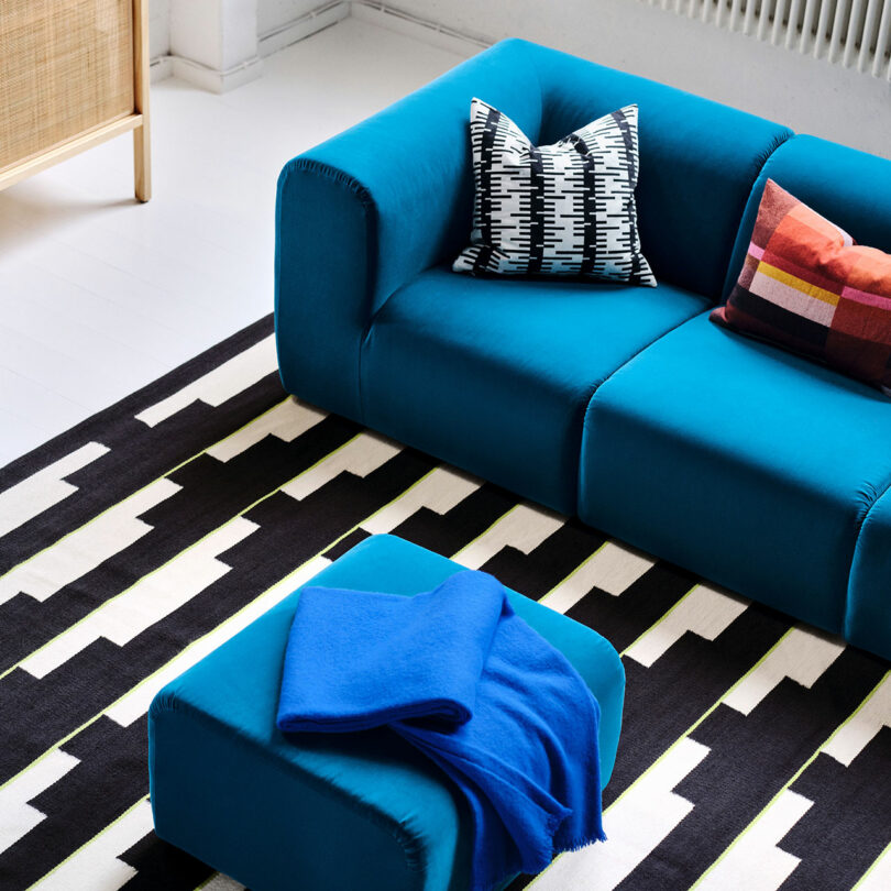 A modern Stockholm IKEA-inspired living room with a blue sofa, patterned black and white rug, colorful cushions, and a blue ottoman draped with a blue blanket.
