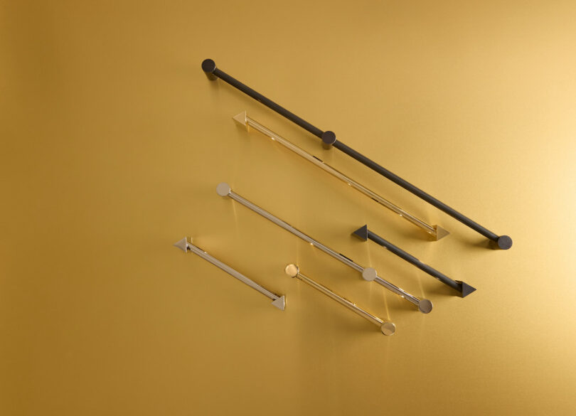 Seven sleek, modern metal rods with various geometric shapes are mounted on a gold-hued wall